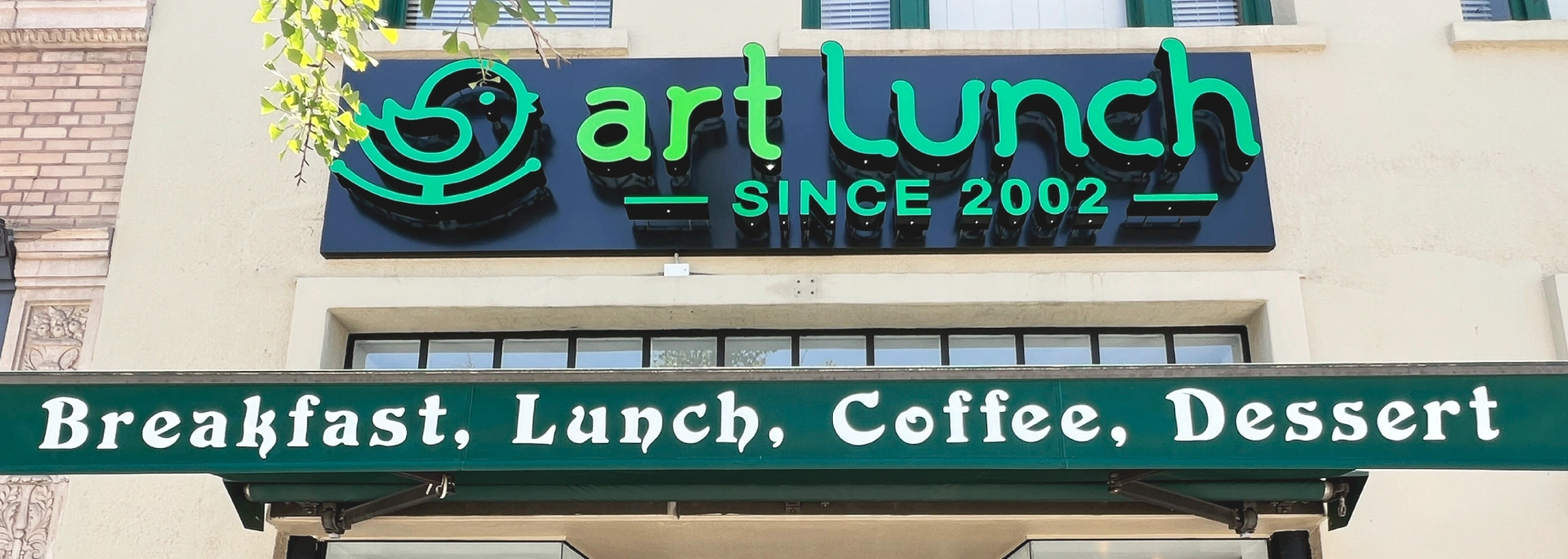 Art Lunch restaurant sign with green logo and text 'SINCE 2002'. Below, a green awning reads 'Breakfast, Lunch, Coffee, Dessert'.