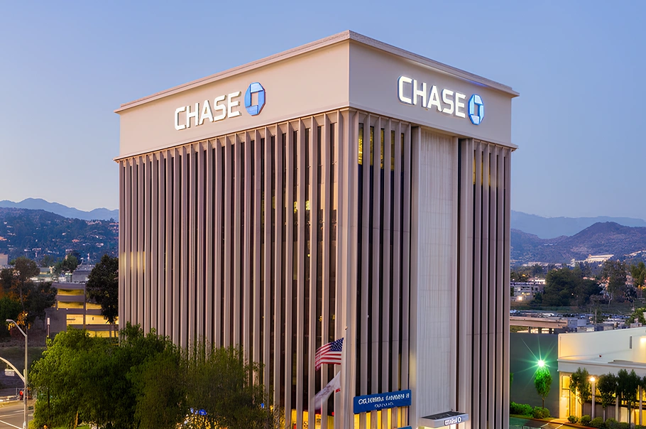 Modern Chase Bank building at dusk with 'CHASE' illuminated signs. An American flag and California flag fly below.